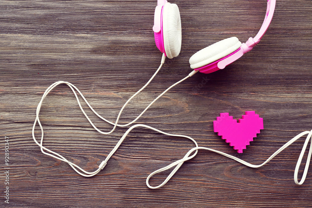 Pink headphones with rosy heart on wooden background Pink headphones with rosy heart on wooden background