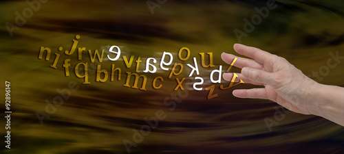 Understanding Dyslexia Website Banner -  female hand with the alphabet flowing from fingers in gold with six letters flipped in white to symbolize dyslexia  photo