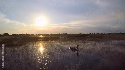 Aerial of a couple enjoying a ride on a Mokono, a traditional canoe in the Okavango Delta swamps at sunset.