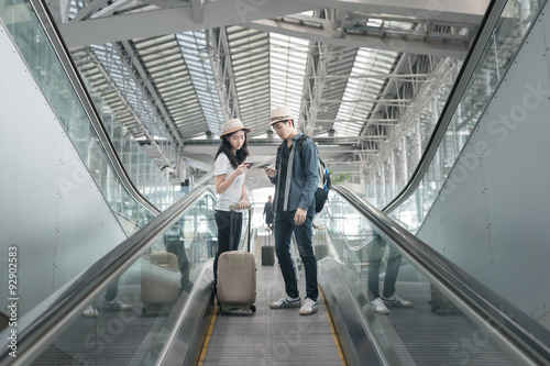 Young asian couple with luggage down the escalator in airport