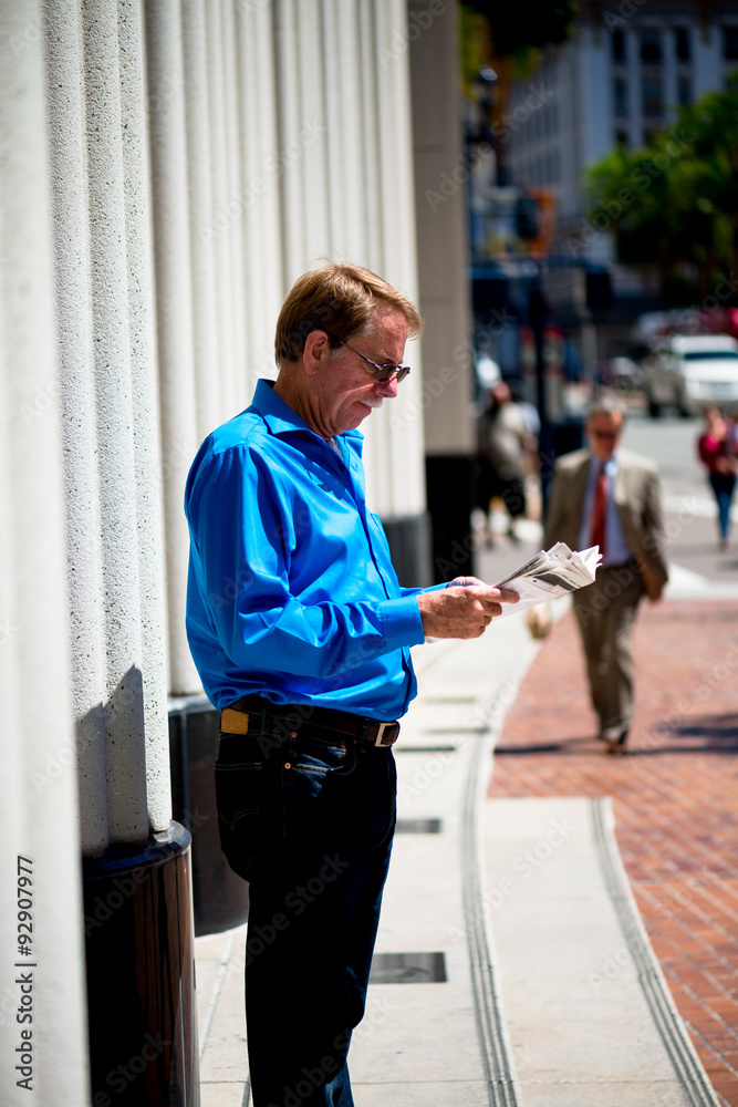 Caucasian male standing in an urban area, reading the newspaper.
