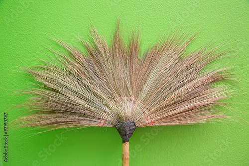 Brown grass broom on green wall background