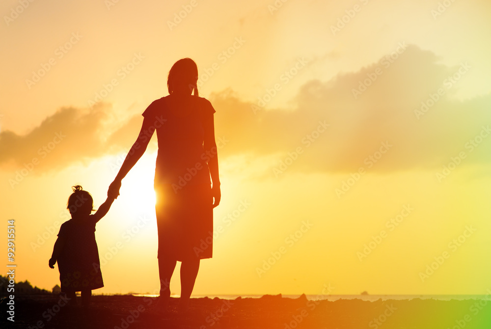 mother and little daughter walking on beach at sunset