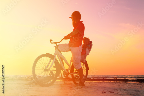 Silhouette of father and baby biking at sunset