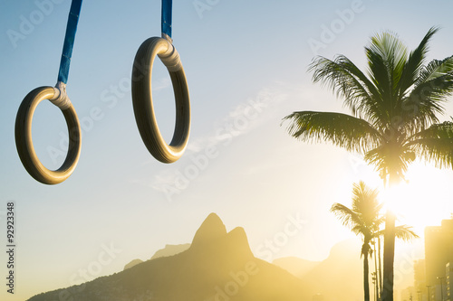 Gymnast rings hanging in golden sunset light above Ipanema Beach at the Rio de Janeiro, Brazil mountain skyline