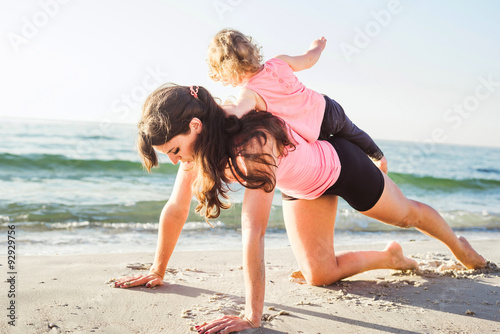 family workout - mother and daughter doing exercises on beach. H