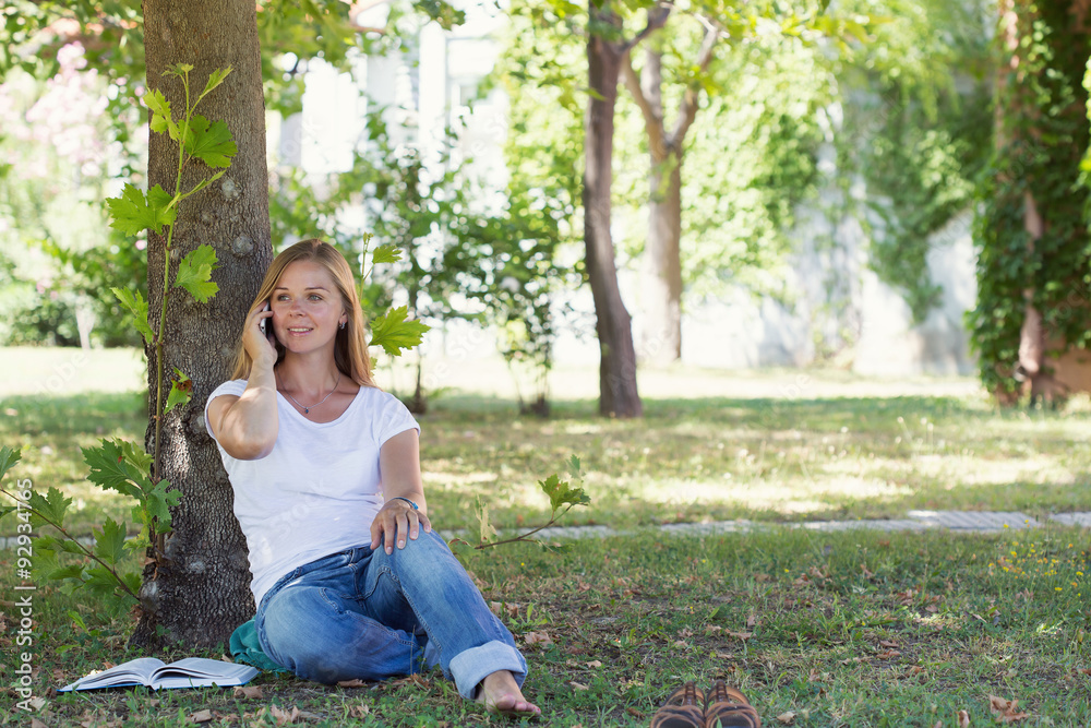 A beautiful blonde woman sitting in a park and talking by the phone A beautiful blonde woman sitting in a park and talking by the phone