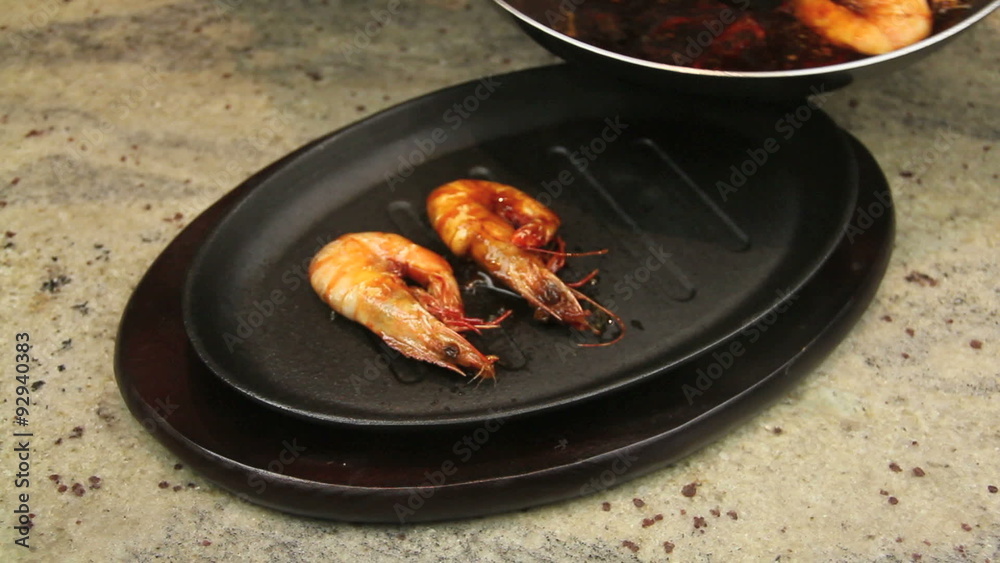 Fried shrimps being put in a baked hot iron pan and sizzling with asian marinade being poured on Fried shrimps being put in a baked hot iron pan and sizzling with asian marinade being poured on