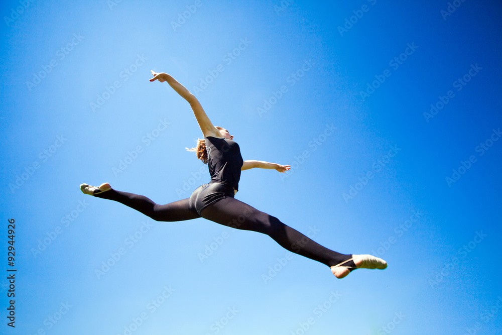 Fototapeta premium Smiling young gymnast is jumping in split and floating above the