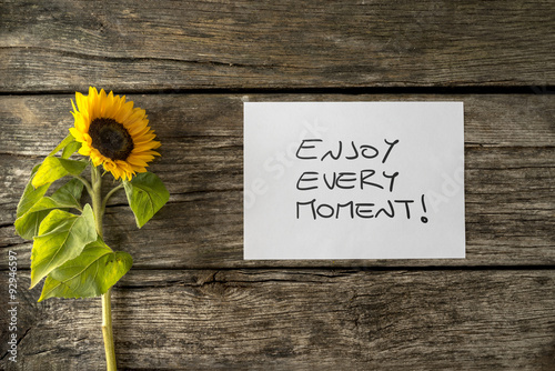 Fototapeta Naklejka Na Ścianę i Meble -  White card with an Enjoy every moment message lying next to a be
