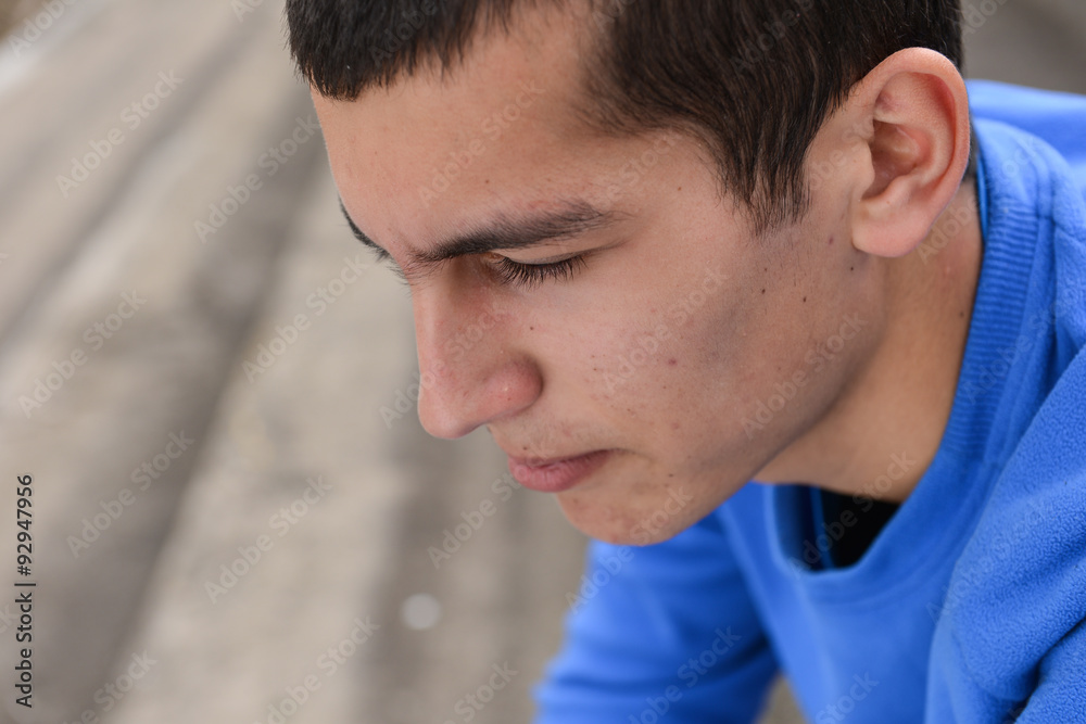 Obraz premium Close up of an unhappy teenage student sitting outside on stadiu