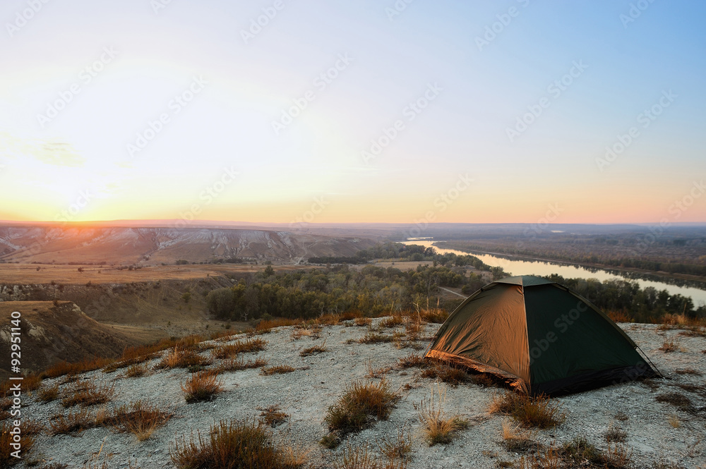 Tent on the hill and river at sunset.