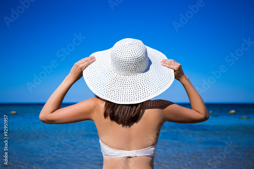 back view of slim woman in bikini and hat looking at the sea