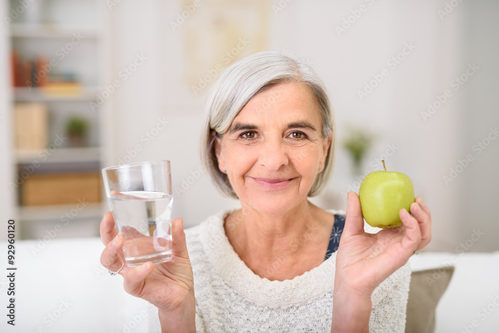 seniorin hält ein glas wasser und einen grünen apfel in der hand seniorin hält ein glas wasser und einen grünen apfel in der hand