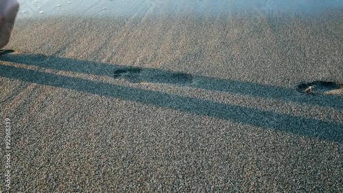 Woman's legs leaving footprint on the sand erasing wave