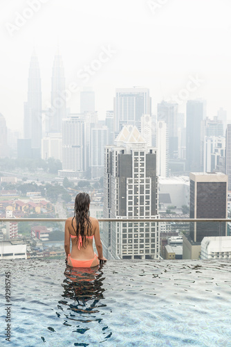 Beautiful woman in swimming pool watching the city