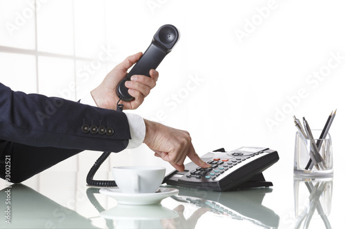 Businessman hands dialing out on a black deskphone