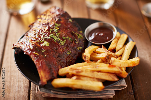 half rack of barbecue pork ribs with french fries on plate