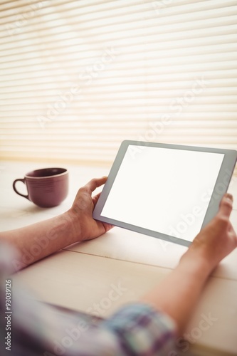  Hands holding digital tablet by coffee cup on table