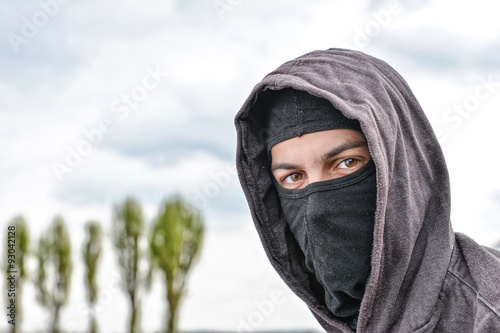 unrecognizable young man wearing black balaclava sitting on old