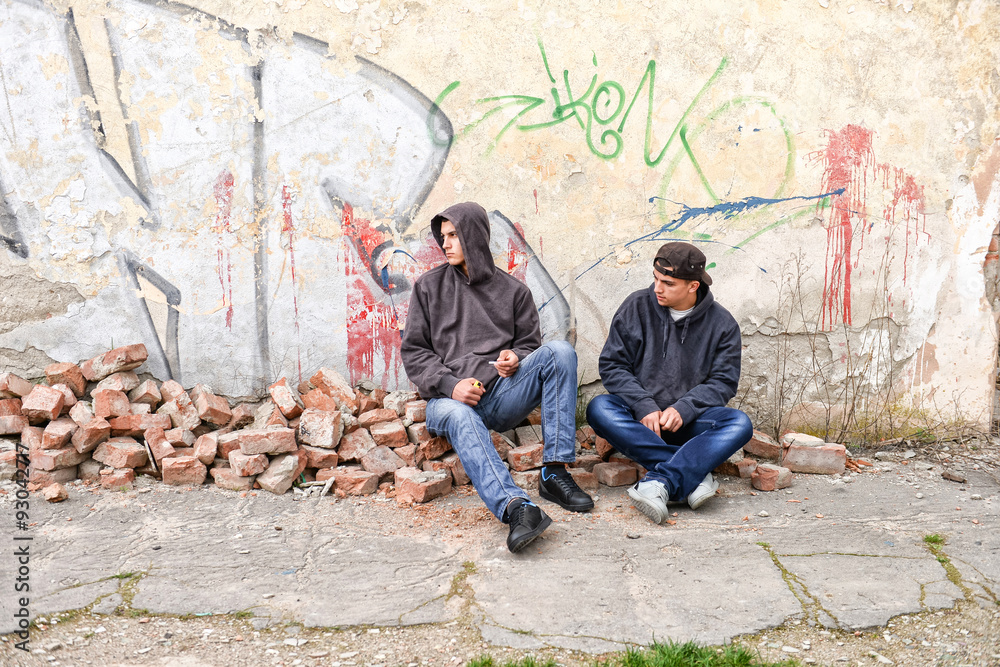 two street hooligans or rappers standing against a graffiti painted wall are preparing to smoke a cigarette two street hooligans or rappers standing against a graffiti painted wall are preparing to smoke a cigarette
