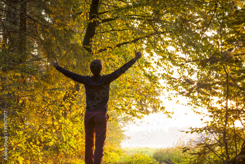 Young man standing on the edge of forested area raising his arms