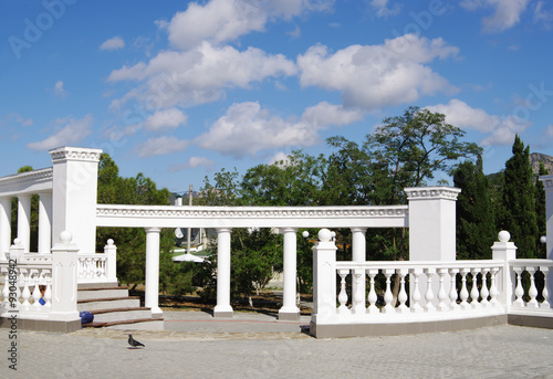 White colonnade in Greek style on blue sky in clouds, entrance to park of township Sudak, Crimea, Russia 