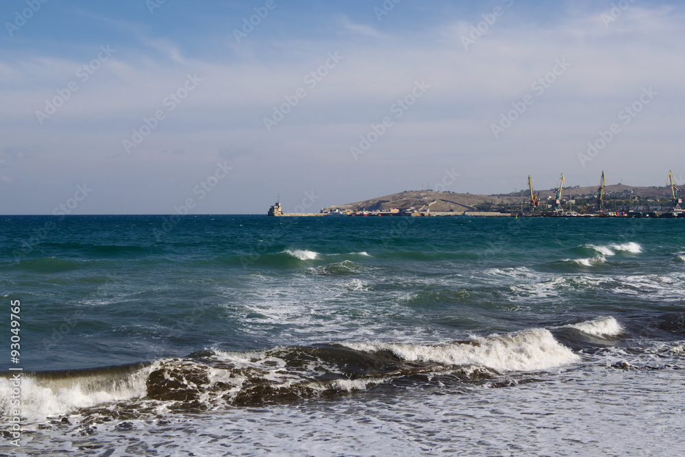 Sea waves with white crests lapping on shore closeup, marine port on back plane,
   Feodosiya, Crimea  