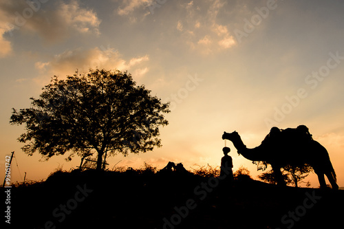 Silhouette of the Camel Trader crossing the sand dune during sun photo