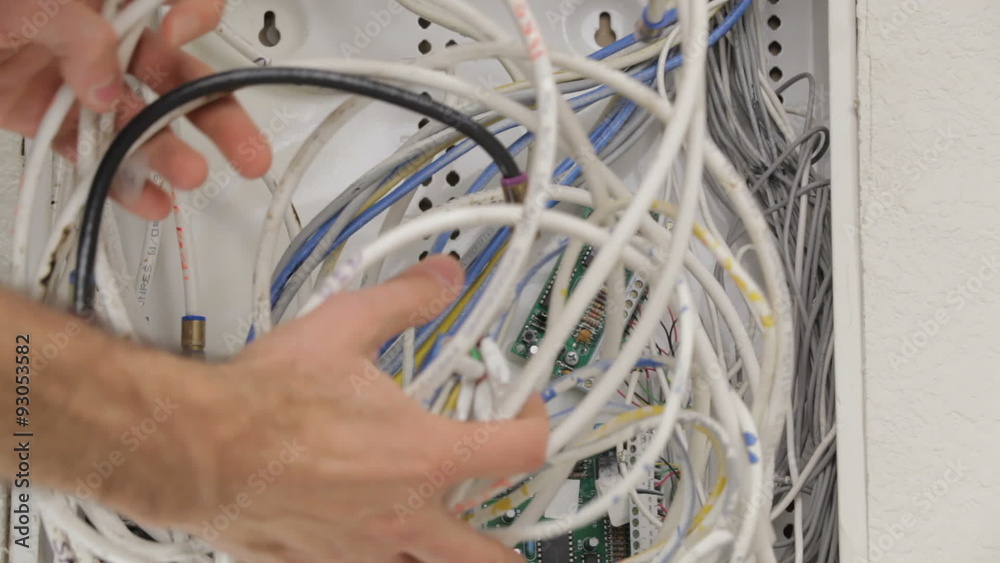 Man moving around a tangle of cables and wires in a home's in-wall structured wiring panel.
