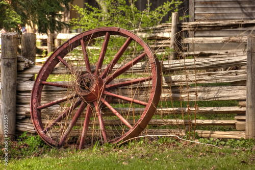 A single rustic wagon wheel leaning against wooden fence.