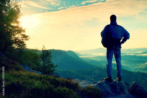 Silhouette of tourist with backpack. Sunny spring daybreak in rocky mountains. Hiker with sporty backpack stand on rocky view point above misty valley. © rdonar