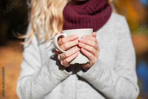 girl holding a mug of tea in the autumn park