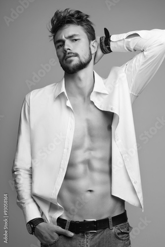 Portrait of a beautiful athletic man in white shirt and jeans in the studio, black and white photo
