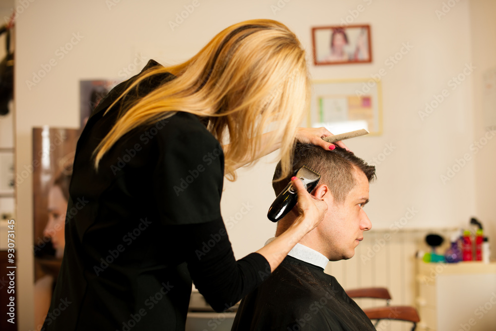 Fototapeta premium Female hairdresser cutting hair of smiling man client at beauty