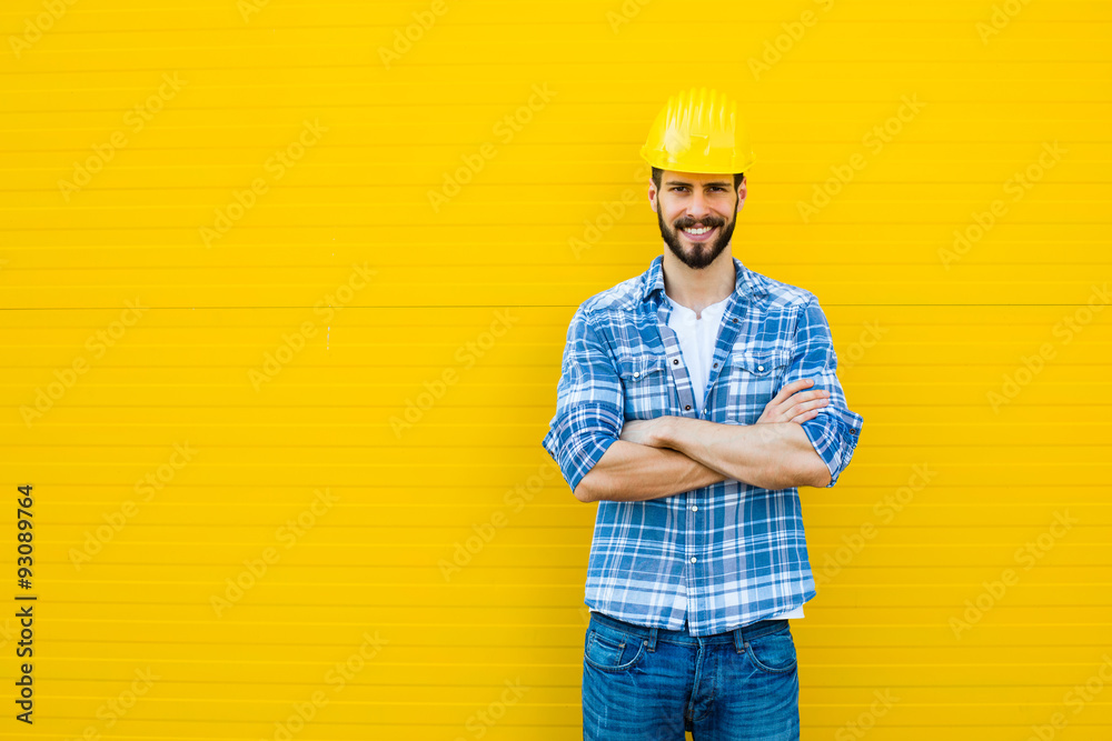 adult worker with helmet on yellow wall - obrazy, fototapety, plakaty 