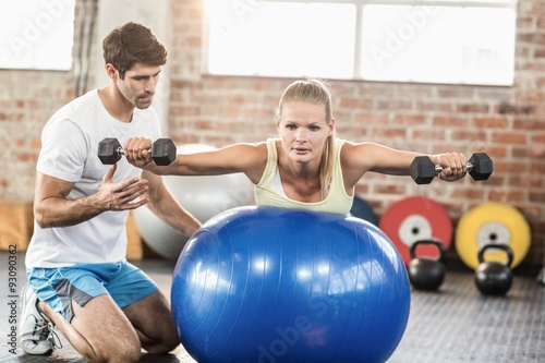 Male trainer helping young woman with the dumbbells 