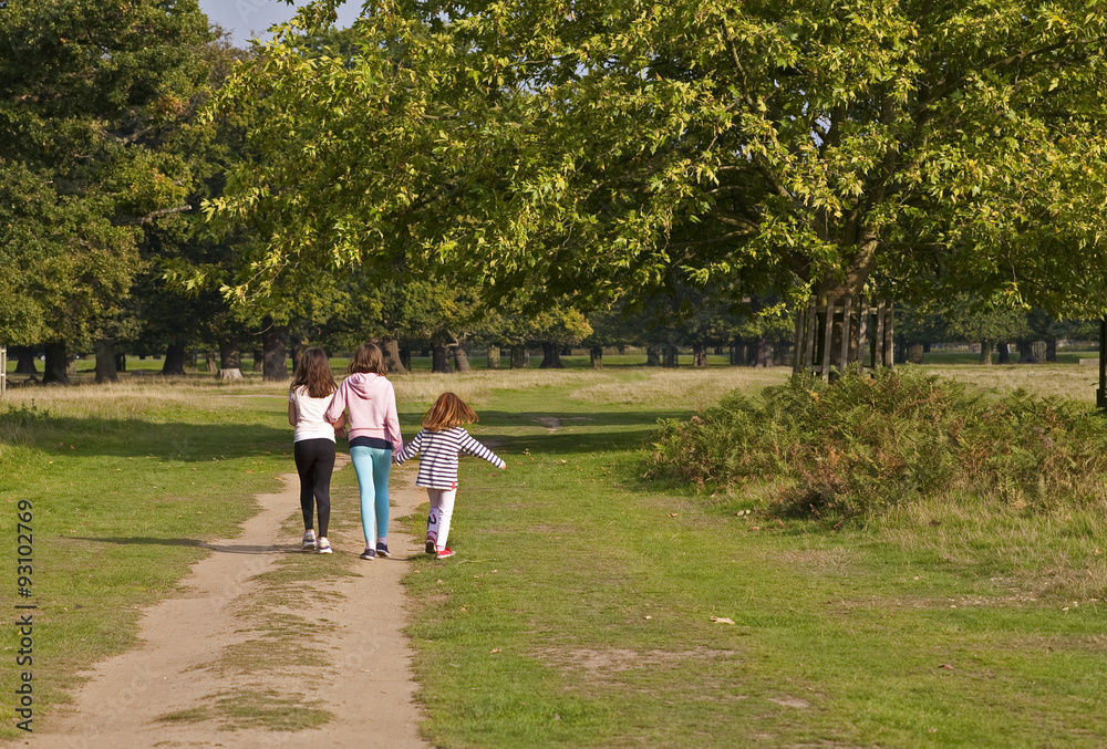 With a Twirl of my Hair. Three young girls set off  down a path into the park. The youngest is dancing and this has set her hair twirling.