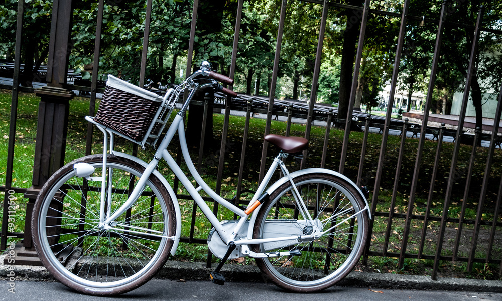 Traditional dutch white  bicycle with crib, bell and  headlight   parked at the front of metal fence