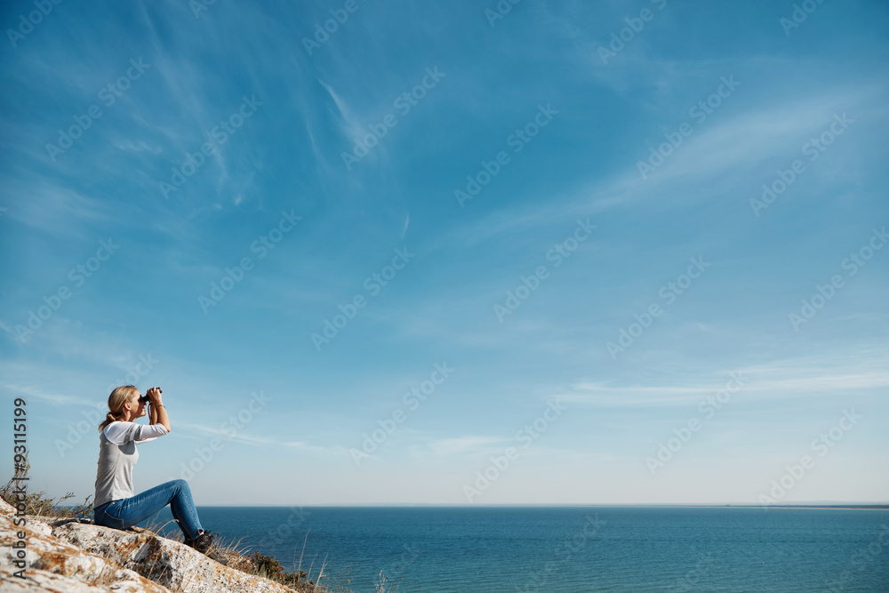 Young active female standing on the top of mountain and watching away in binocular, extreme lifestyle, traveling and trek concept, copy space Young active female standing on the top of mountain and watching away in binocular, extreme lifestyle, traveling and trek concept, copy space