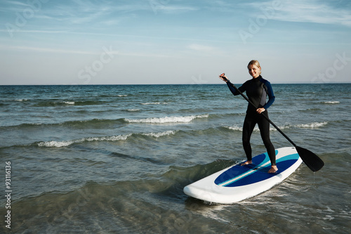 Photography Young blonde female paddles a paddleboard at the sea .