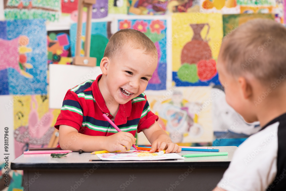 Fototapeta premium Cute happy toddler boys is at the Art class. Paint something with markers, laughing and just have fun. Colorful wall with paintings in background.