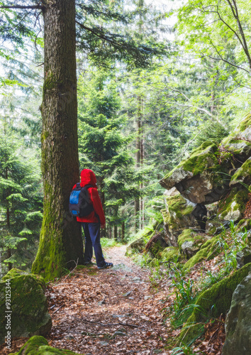 Man wearing red raincoat and a rucksack hiking in mountain forest in summer. Vintage effect