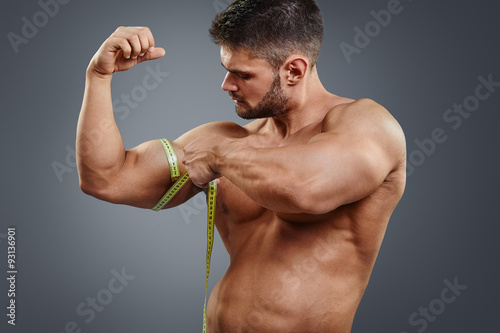 Tela Closeup handsome strong athlete measuring muscle biceps with tape measure isolated over gray background