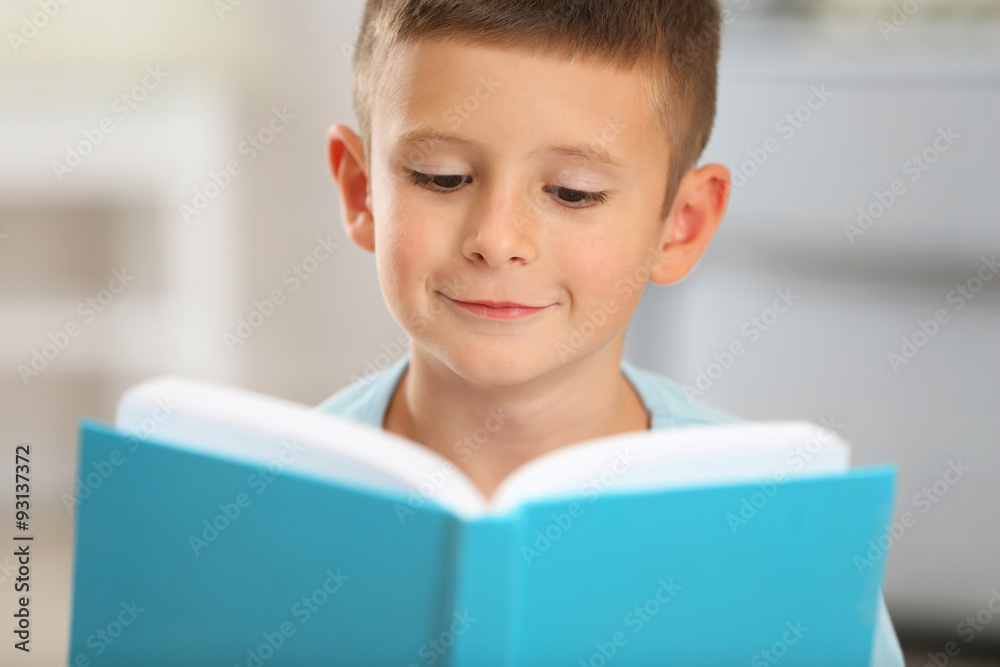 Little boy with book sitting on carpet, on home interior background Little boy with book sitting on carpet, on home interior background