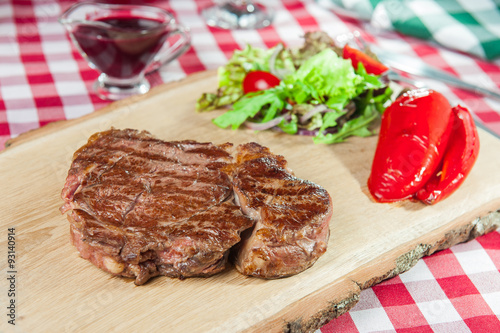  Ribeye steak with vegetable salad pillow, roasted bell pepper and sauce on the wood board on the served restaurant table