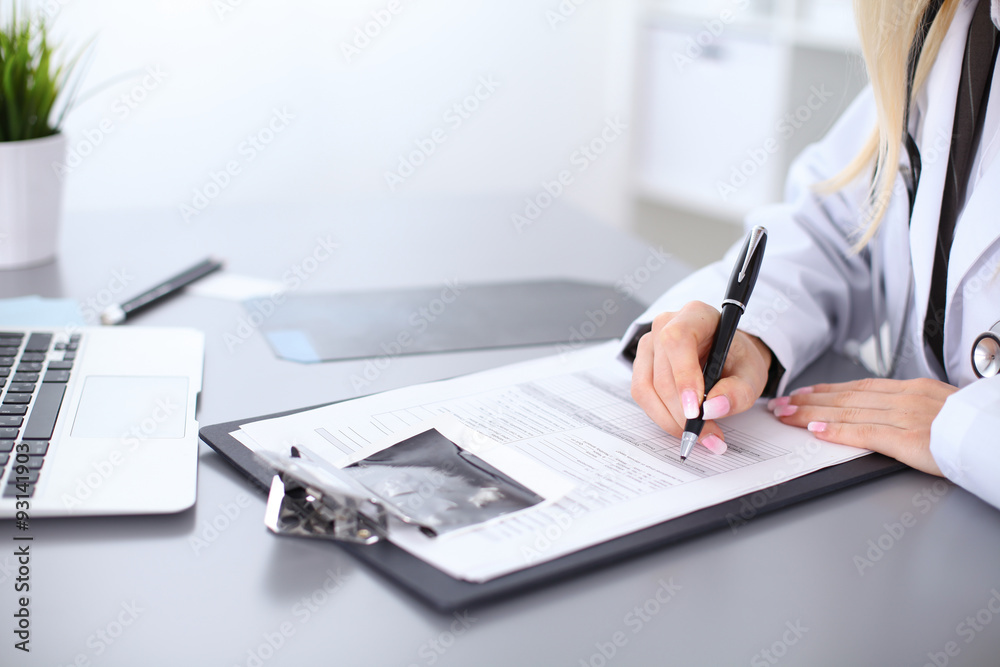 Close up of female doctor filling up a medical history form, sitting at the table in hospital Close up of female doctor filling up a medical history form, sitting at the table in hospital