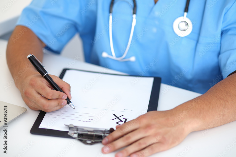Portrait of unknown male surgeon doctor holding his stethoscope and filling up medical prescription Portrait of unknown male surgeon doctor holding his stethoscope and filling up medical prescription