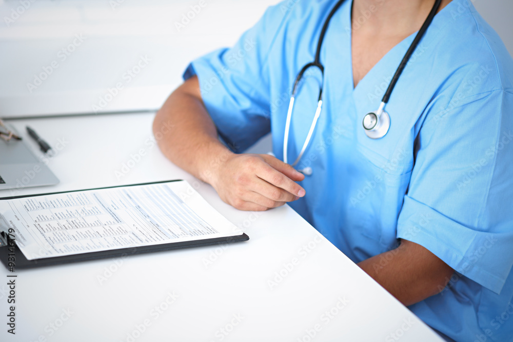 Portrait of unknown male surgeon doctor sitting at the table in hospital office, stethoscope Portrait of unknown male surgeon doctor sitting at the table in hospital office, stethoscope