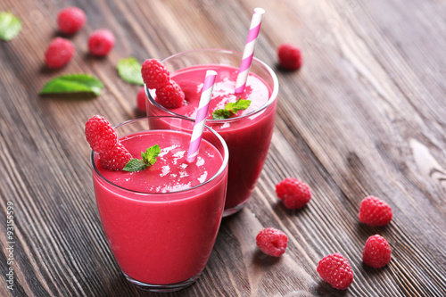 Glasses of raspberry milk shake with berries on wooden table close up